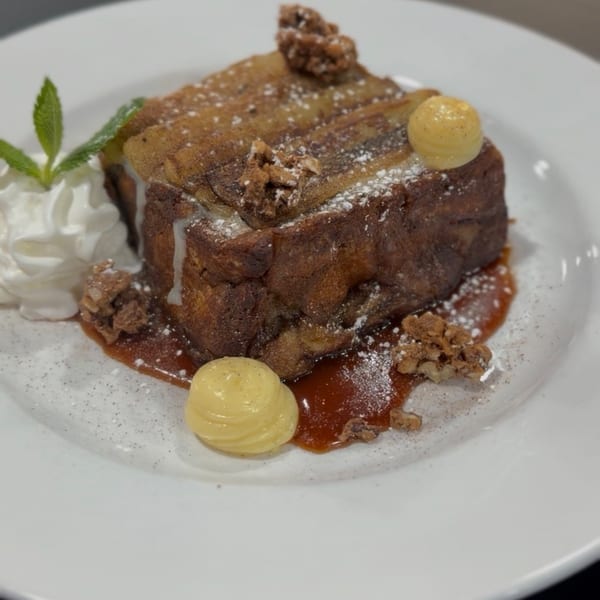 Thick French toast with caramel, whipped cream, mint, nuts, and two dollops of cream.