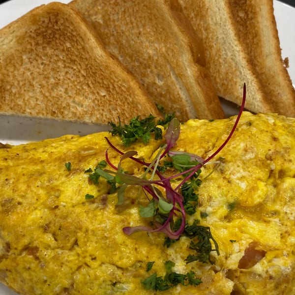 A fluffy omelet topped with microgreens and parsley, served with two slices of golden-brown toast.