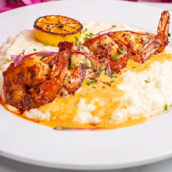 Shrimp and grits with a grilled lemon slice, garnished with chives and microgreens.