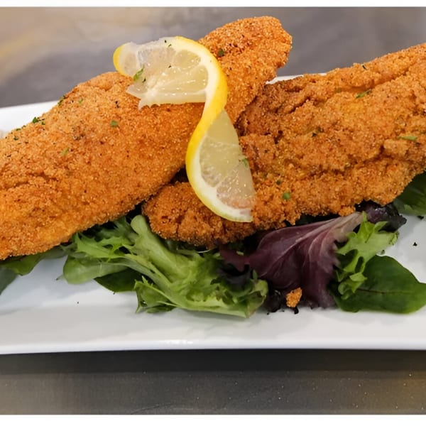 Two pieces of crispy fried fish, garnished with lemon slices and fresh greens on a white plate.