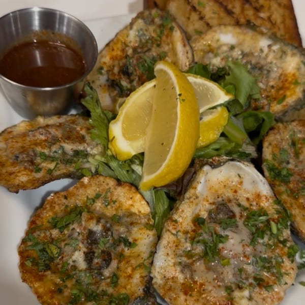 Grilled oysters topped with herbs, served with lemon wedges, cocktail sauce, and toast.