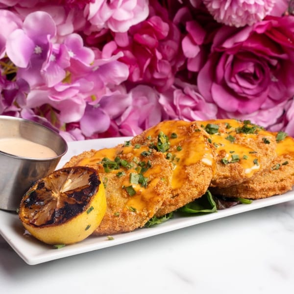 Three golden-fried green tomatoes topped with sauce and chives, served with a grilled lemon and dip.