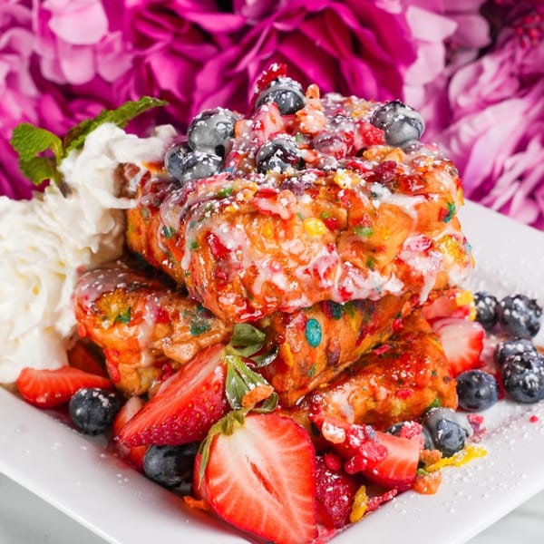 French toast topped with berries, whipped cream, powdered sugar, and colorful cereal bits.