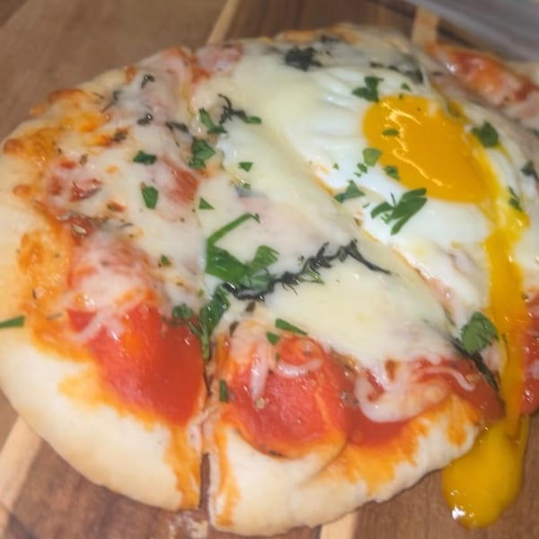 Breakfast pizza with melted cheese, pepperoni, herbs, and a runny fried egg on a wooden board.