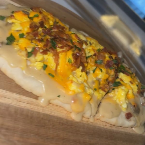 A breakfast dish from Toast It IZ, featuring scrambled eggs, cheese, bacon, and gravy on toast.