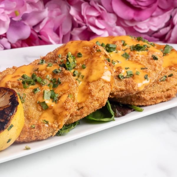 Fried green tomatoes with orange sauce and green garnish, served with a grilled lemon.