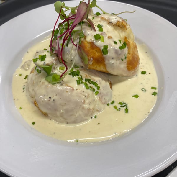 Biscuits and gravy, garnished with chives and microgreens, served on a white plate.