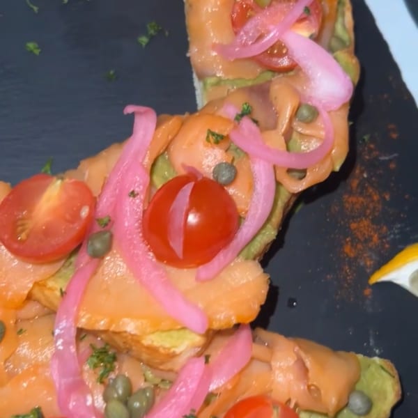 Close-up of Toast It IZ avocado toast with smoked salmon, pickled red onions, capers, and cherry tomatoes.