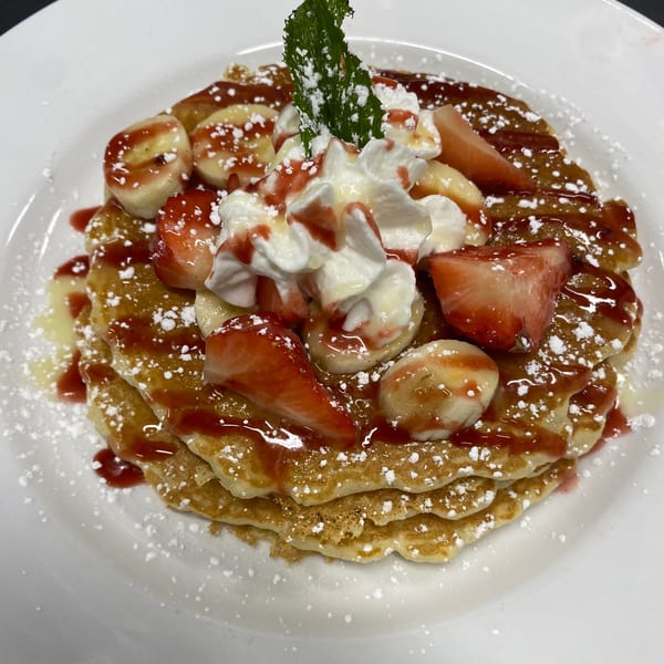 Fluffy pancakes topped with strawberries, bananas, whipped cream, syrup, and powdered sugar.