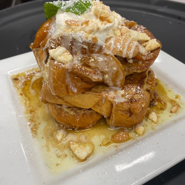 Golden French toast stack, drizzled with syrup and icing, topped with whipped cream, mint, and crumbles.