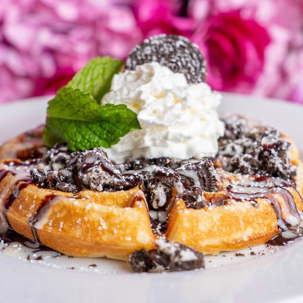Golden waffle topped with whipped cream, Oreo crumbles, chocolate drizzle, powdered sugar, and mint.