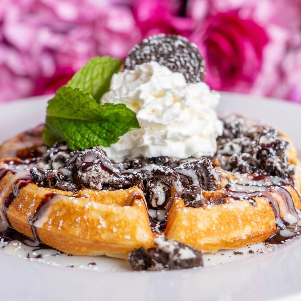 Golden waffle topped with whipped cream, Oreo crumbles, chocolate drizzle, powdered sugar, and mint.